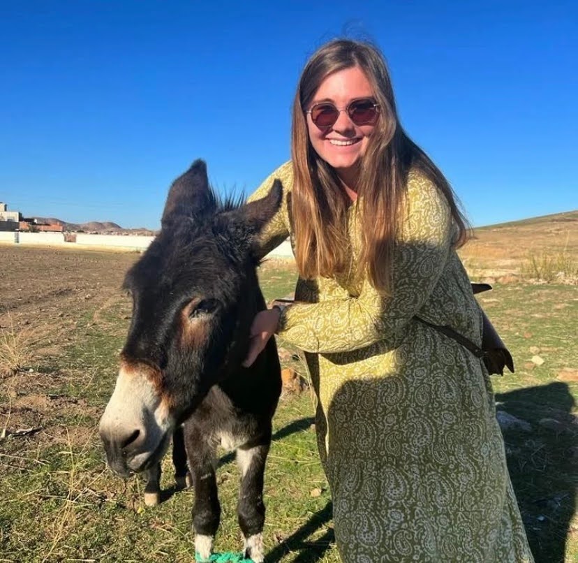 Destiny Prinski smiles into the camera next to a dark grey donkey.